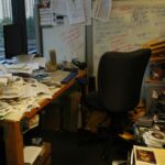 Unordentlicher Schreibtisch im Homeoffice mit Papieren, Büchern und CDs – Beispiel für fehlende Ordnung am Arbeitsplatz.